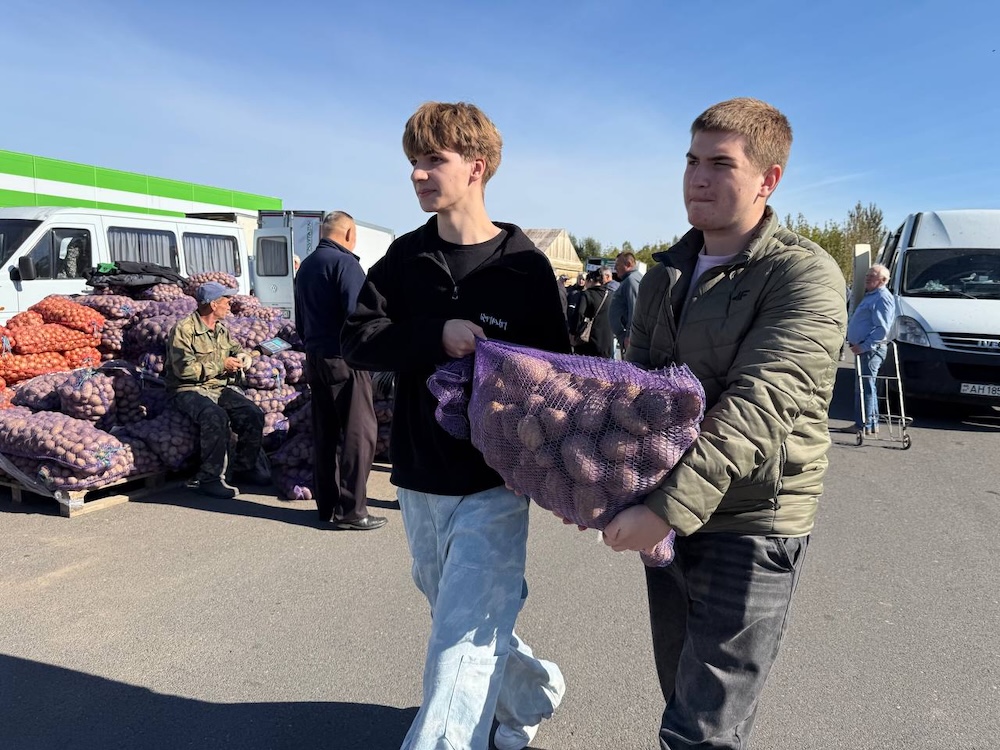 Молодые люди несут мешок картошки на осенней сельскохозяйственной ярмарке в Бресте